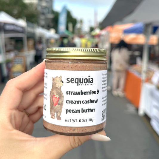 Hand holding a jar of sequoia pecan butter at an outdoor market.